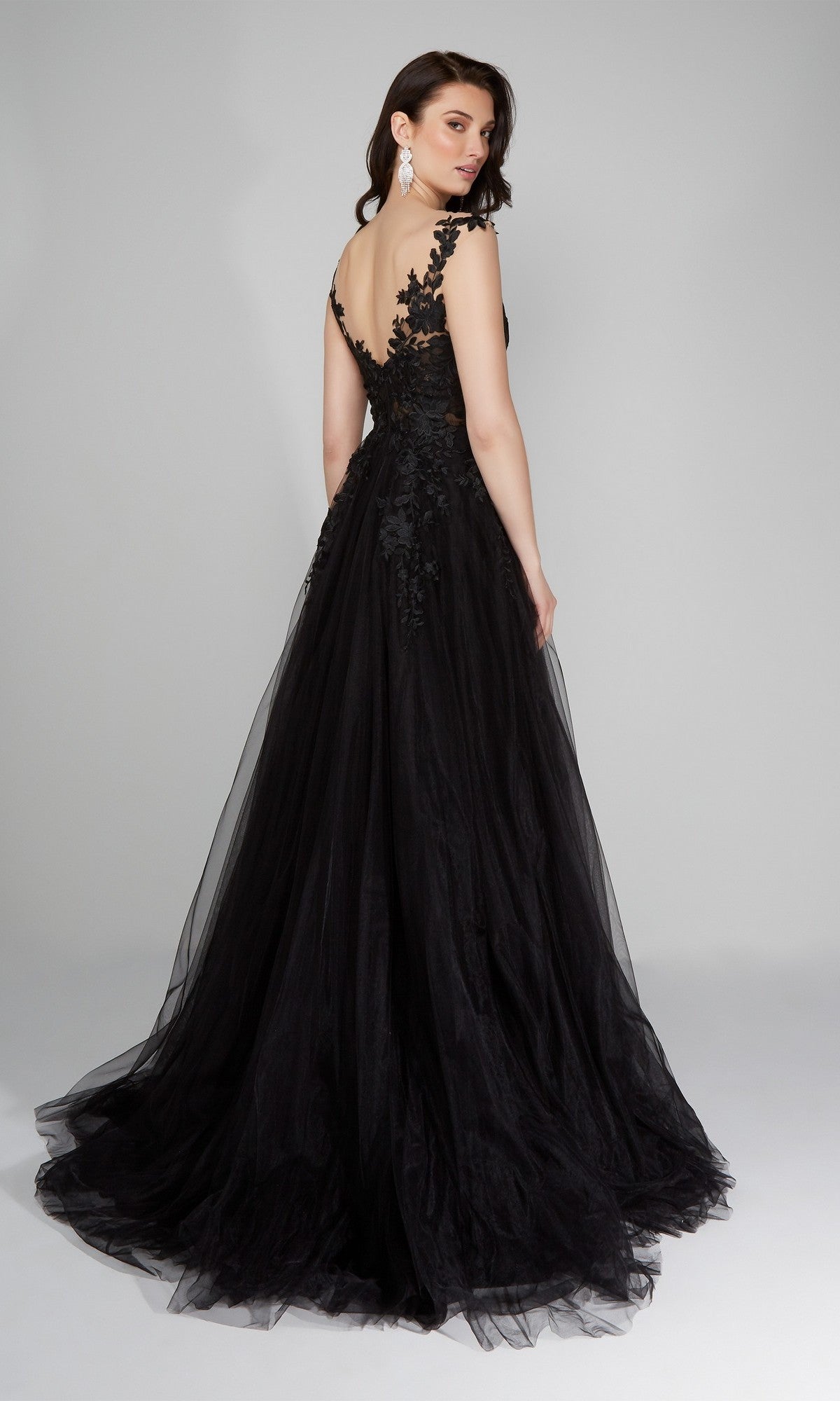 Wearing the Alyce 5090 long formal dress, a woman poses against a plain gray background in a black lace embroidered gown featuring a deep V-back and an elegant A-line tulle skirt.